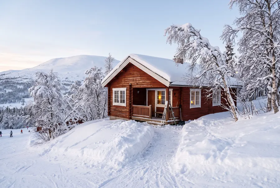 Exempelbild: röd fjällstuga med vita knutar i djup snö, med fjället bakom