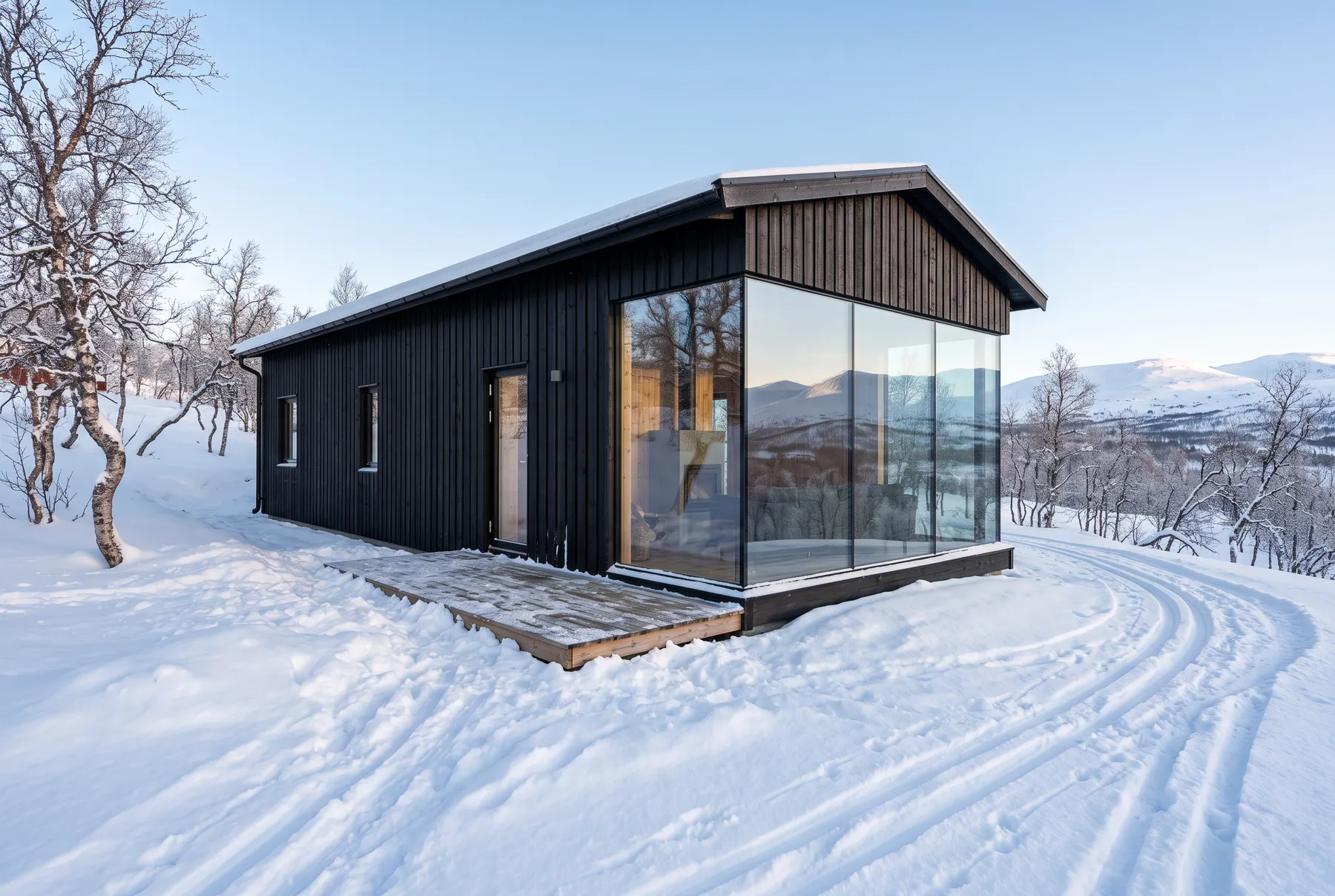 Exempelbild: modern svart stuga med ett hörn i glas, i snön mellan björkarna